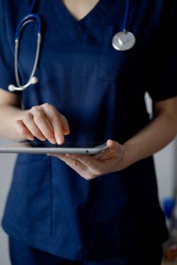 Doktor kadın panorama penceresinin yanında dururken tablet bilgisayar kullanıyor, kapatın. Doktor ya da cerrah iş başında. Tıp konsepti.