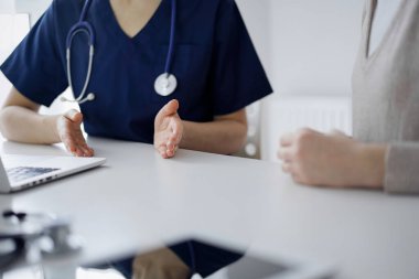 Doktor ve hasta, klinikteki masada el ele otururken sağlık muayenesi sırasında birbirleriyle konuşuyorlar. Mükemmel tıbbi hizmet ve tıp konsepti.