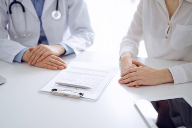 Doktor ve hasta birbirlerine yakın otururken sağlık sorularını tartışıyorlar ve klinikteki masada pano kullanıyorlar, sadece ellerini kapatıyorlar. Tıp konsepti.
