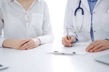 Doktor ve hasta klinikteki masada yan yana oturuyorlar. Kadın doktorların ellerinin tıbbi geçmiş kayıtlarını doldurması ya da kontrol listesi üzerinde yoğunlaşacağız. Kapat. Tıp konsepti.