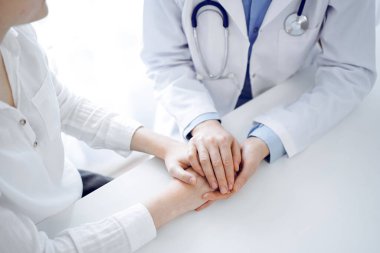 Doktor ve hasta klinikteki masada yan yana oturuyorlar. Kadın doktorlara odaklan. Kadına güven veren eller, sadece eller, yakın çekim. Tıp konsepti.