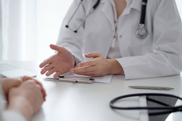 Doctor and patient discussing current health questions while sitting at the desk in clinic office, closeup. Medicine and healthcare concept.