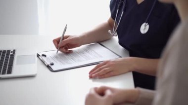 Doktor ve hasta klinikteki yetenek penceresinin yanındaki beyaz masada oturup test sonuçlarını tartışıyor. Bilinmeyen doktor tıbbi kayıt formlarını doldurmak için pano kullanıyor. Tıp konsepti.