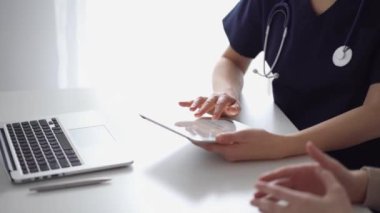 Doktor ve hasta klinikteki özel pencerenin yanındaki beyaz masada oturuyorlar. Bilinmeyen kadın doktor tıbbi kayıt formlarını doldurmak için tablet bilgisayar kullanıyor. Tıp konsepti.