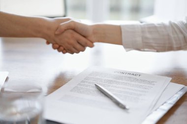 İş adamları kontrat kağıtlarının üzerinde el sıkışıyor. Tahta masaya yeni imzalanmış. Kapatın. Toplantıdaki avukatlar. Takım çalışması, ortaklık, başarı kavramı.