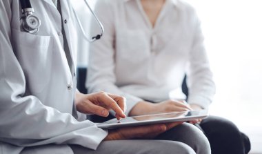 Doktor ve hasta klinikteki koltukta oturuyor. Tablet bilgisayar kullanan kadın doktorların ellerine odaklan, kapat. Mükemmel tıbbi hizmet ve tıp konsepti.
