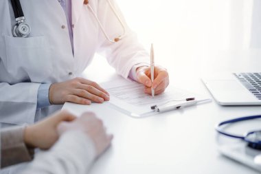 Doktor ve hasta klinikteki masada oturuyor. Kadın doktorların ellerinin tıbbi geçmiş kayıtlarını doldurması ya da kontrol listesi üzerinde yoğunlaşacağız. Kapat. Tıp konsepti.