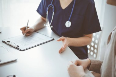 Doktor ve hasta klinikteki masada oturmuş bir şey tartışıyorlar. Kadın doktorların ellerine odaklan, yakın çekim. Tıp konsepti.