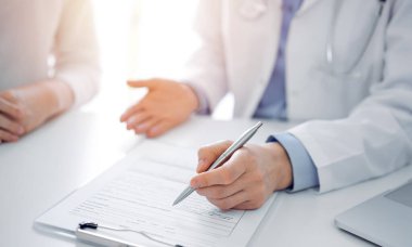 Doktor ve hasta birbirlerine yakın otururken sağlık sorularını tartışıyorlar ve klinikteki masada pano kullanıyorlar, sadece ellerini kapatıyorlar. Tıp konsepti.