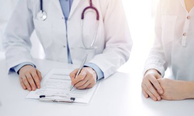Doktor ve hasta klinikteki masada yan yana oturuyorlar. Kadın doktorların ellerinin tıbbi geçmiş kayıtlarını doldurması ya da kontrol listesi üzerinde yoğunlaşacağız. Kapat. Tıp konsepti.