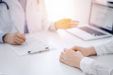 Doktor ve hasta klinikteki masada karşılıklı otururken tablet bilgisayar kullanıyorlar. Doktorun yanındaki kadın ellerine odaklan, yakın çekim. Tıp konsepti.