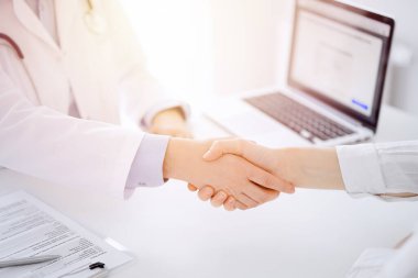 Klinikteki masada karşılıklı otururken doktor ve hasta el sıkışıyor. Sadece eller kapalı. Tıp konsepti.