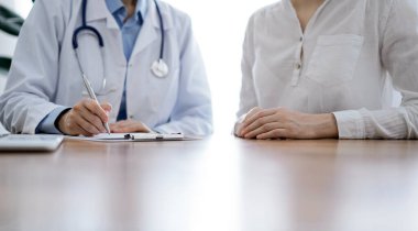 Doktor ve hasta klinikteki ahşap masada yan yana oturuyorlar. Kadın doktorlar kayıt formunu dolduruyorlar. Tıp konsepti.