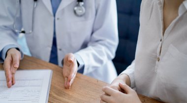 Doktor ve hasta, yukarıdan bakıldığında, klinikteki ahşap masada yan yana otururken bir şeyler tartışıyorlar. Tıp konsepti.