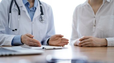 Doktor ve hasta, klinikteki ahşap masada yan yana otururken ellerini kapatarak bir şey tartışıyorlar. Tıp konsepti.