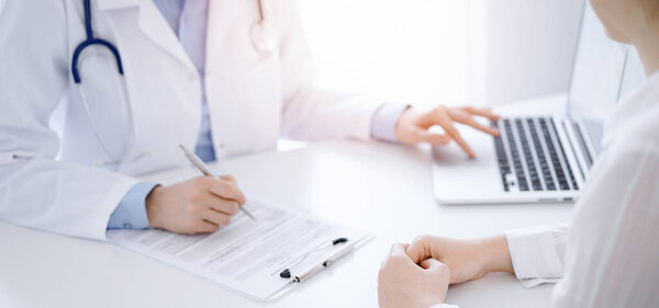 Doctor and patient discussing something and using laptop while sitting opposite each other at the desk in clinic office. Perfect medical service and medicine concept.