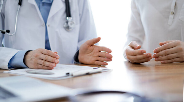 Doctor and patient discussing something while sitting near each other at the wooden desk in clinic. Medicine concept.