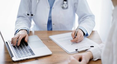 Doktor ve hasta klinikteki ahşap masada oturuyorlar. Dizüstü bilgisayar monitörüne bakan kadın doktorlar, kapatın. Tıp konsepti.