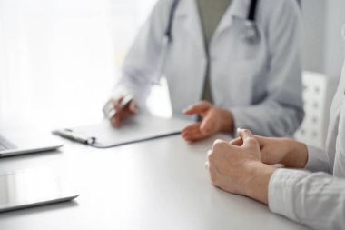 Doktor ve hasta klinikteki masada otururken sağlık muayenesini tartışıyorlar. Kadın hastaların ellerine odaklan, kapat. Mükemmel tıbbi hizmet ve tıp konsepti.