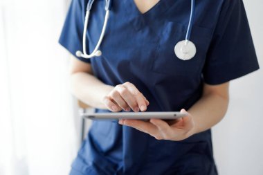 Doktor kadın panorama penceresinin yanında dururken tablet bilgisayar kullanıyor, kapatın. Doktor ya da cerrah iş başında. Tıp konsepti.