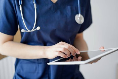 Doktor kadın panorama penceresinin yanında dururken tablet bilgisayar kullanıyor, kapatın. Doktor ya da cerrah iş başında. Tıp konsepti.