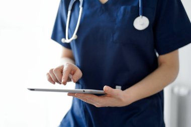 Doktor kadın panorama penceresinin yanında dururken tablet bilgisayar kullanıyor, kapatın. Doktor ya da cerrah iş başında. Tıp konsepti.