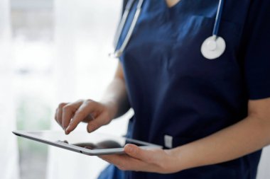 Doktor kadın panorama penceresinin yanında dururken tablet bilgisayar kullanıyor, kapatın. Doktor ya da cerrah iş başında. Tıp konsepti.