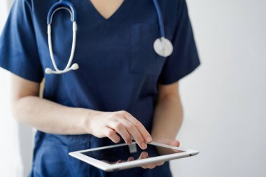 Doktor kadın panorama penceresinin yanında dururken tablet bilgisayar kullanıyor, kapatın. Doktor ya da cerrah iş başında. Tıp konsepti.