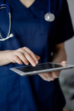 Doktor kadın panorama penceresinin yanında dururken tablet bilgisayar kullanıyor, kapatın. Doktor ya da cerrah iş başında. Tıp konsepti.