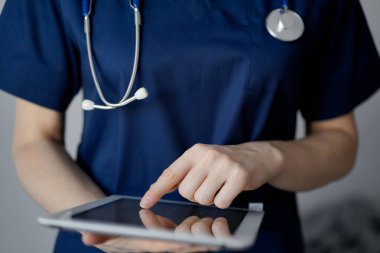 Doktor kadın panorama penceresinin yanında dururken tablet bilgisayar kullanıyor, kapatın. Doktor ya da cerrah iş başında. Tıp konsepti.