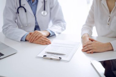 Doktor ve hasta birbirlerine yakın otururken sağlık sorularını tartışıyorlar ve klinikteki masada pano kullanıyorlar, sadece ellerini kapatıyorlar. Tıp konsepti.
