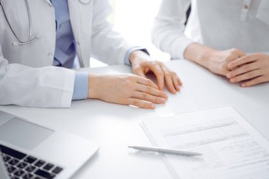 Doktor ve hasta birbirlerine yakın otururken sağlık sorularını tartışıyorlar ve klinikteki masada pano kullanıyorlar, sadece ellerini kapatıyorlar. Tıp konsepti.