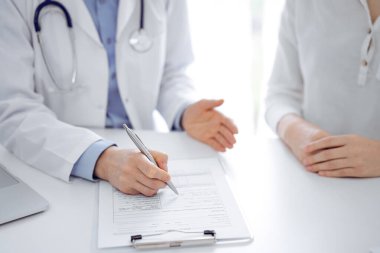 Doktor ve hasta birbirlerine yakın otururken sağlık sorularını tartışıyorlar ve klinikteki masada pano kullanıyorlar, sadece ellerini kapatıyorlar. Tıp konsepti.