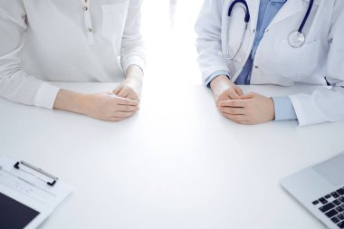 Doktor ve hasta klinikteki masada yan yana oturuyorlar, yakın plan. Tıp konsepti.