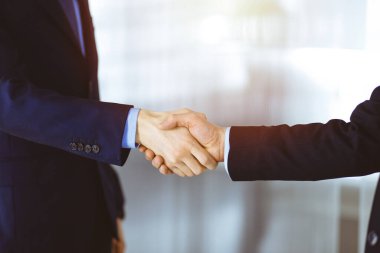 İş adamları el sıkışıyor, yakın plan. Güneşli bir modern ofiste duran bir grup tanınmamış iş adamı. Takım çalışması, ortaklık ve el sıkışma kavramı.