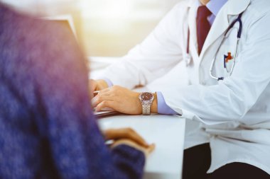Bir doktor, hastanedeki güneşli dolapta birlikte otururken hastasıyla konuşuyor. Doktor ilaç kayıtlarını doldurmak için pano kullanıyor. Mükemmel tıbbi servis.