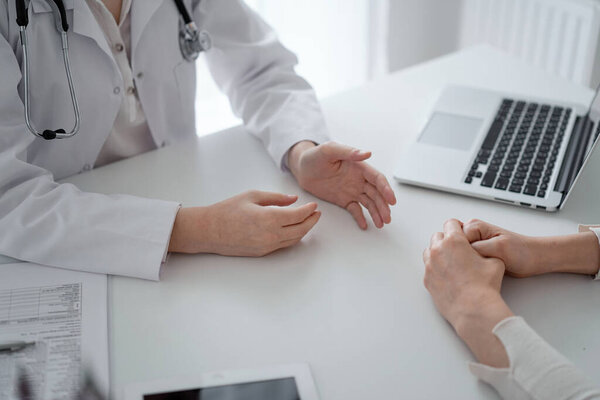 Doctor and patient discussing current health questions while sitting at the desk in clinic office, closeup. Medicine and healthcare concept.