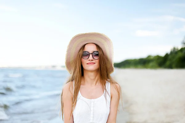 ハッピー笑顔の女性は 海のビーチに立って帽子とサングラスでポーズする幸せな幸せの至福 旅行休暇中に自然を楽しむ白い夏のドレスの女性モデルの肖像 — ストック写真