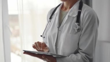 Doktor kadın klinikteki panorama penceresinin yanında dururken tablet bilgisayar kullanıyor. Tıp konsepti.