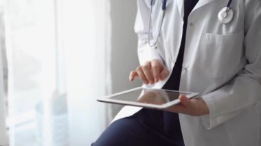 Doktor kadın klinikteki panorama penceresinin yanında dururken tablet bilgisayar kullanıyor. Tıptaki yetenekler.