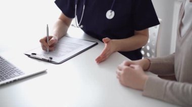 Doktor ve hasta klinikteki yetenek penceresinin yanındaki beyaz masada oturup test sonuçlarını tartışıyor. Bilinmeyen doktor tıbbi kayıt formlarını doldurmak için pano kullanıyor. Tıp konsepti.