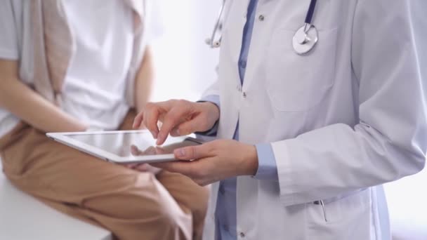 医師はタブレットコンピュータを使い 患者は近くに座っている 未知の医師が働いている 医学と医療のコンセプト — ストック動画