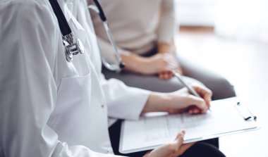 Doktor ve hasta klinikteki koltukta oturuyor. Kadın doktorların ellerinin ilaç geçmişi formunu doldurmasına odaklan, kapat. Tıp konsepti.