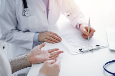 Doktor ve hasta klinikteki masada oturuyor. Kadın doktorların ellerinin tıbbi geçmiş kayıtlarını doldurması ya da kontrol listesi üzerinde yoğunlaşacağız. Kapat. Tıp konsepti.