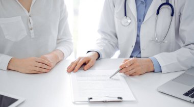 Doktor ve hasta birbirlerine yakın otururken sağlık sorularını tartışıyorlar ve klinikteki masada pano kullanıyorlar, sadece ellerini kapatıyorlar. Tıp konsepti.