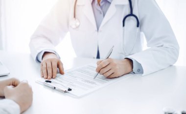 Doktor ve hasta, klinikteki masada karşılıklı otururken mevcut sağlık sorunlarını tartışıyorlar. Sadece ellerinizi yakın plan yapın. Tıp konsepti.