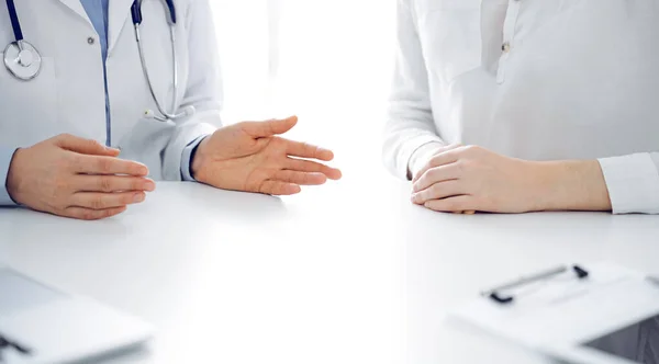 Doctor and patient discussing current health questions while sitting near of each other at the table in clinic, just hands closeup. Medicine concept.