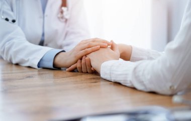 Doktor ve hasta klinikteki ahşap masada oturuyorlar. Kadın doktorların elleri güven veren kadınlarındır. Tıp konsepti.