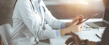 Kimliği belirsiz genç kadın doktor güneşli klinikte birlikte otururken hastasını dinliyor. Coronavirus salgını sırasında ilaç konsepti. Covid 2019.