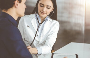 Genç bayan doktor, klinikte yan yana otururken hastalarının kan basıncını kontrol ediyor. Tıp ve sağlık hizmetleri kavramları.